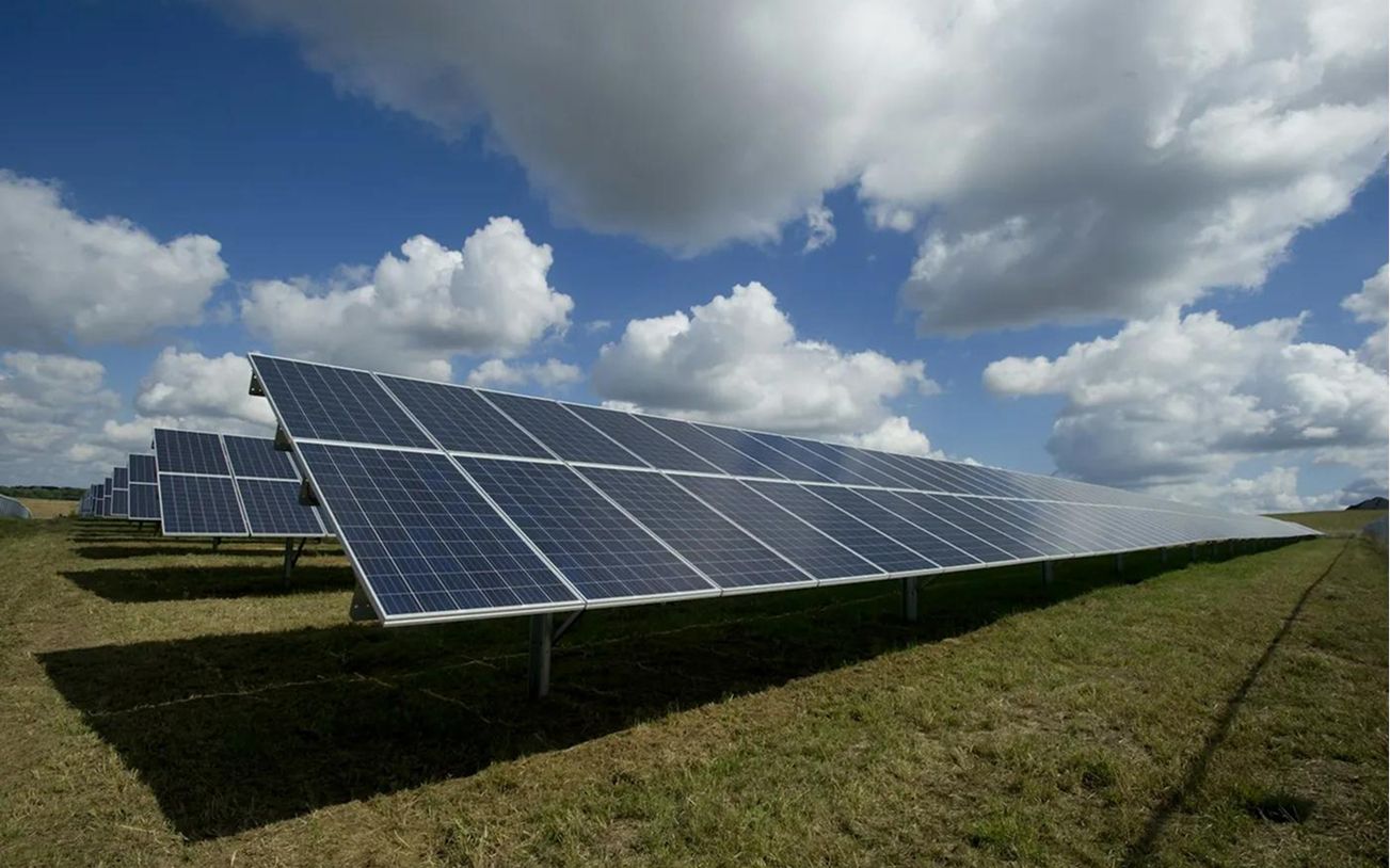Paneles solares en un campo bajo un cielo con nubes