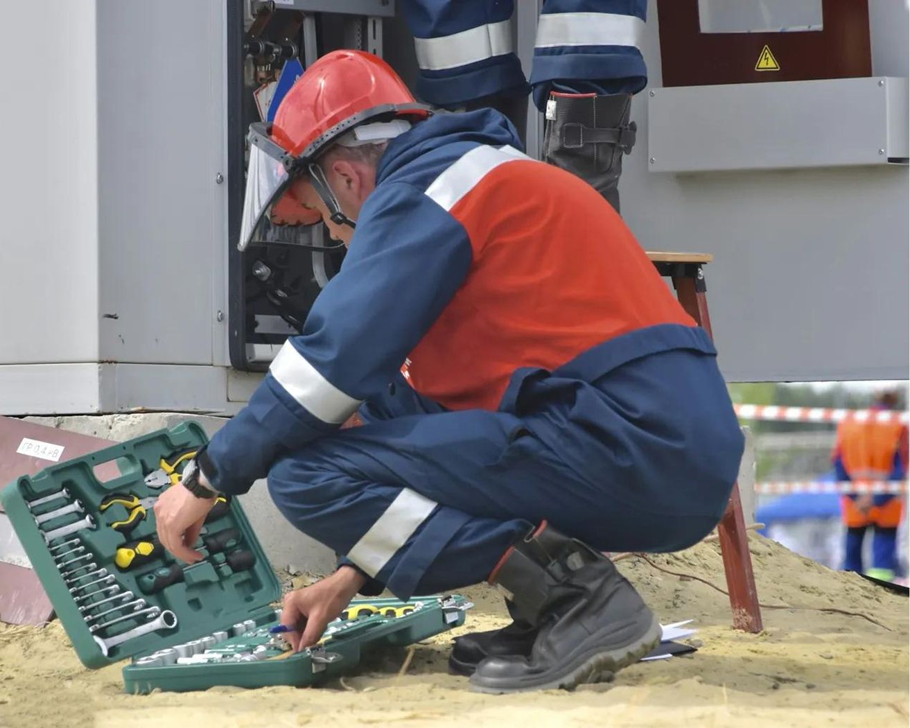 Técnico con equipo de protección preparando herramientas junto a un equipo eléctrico